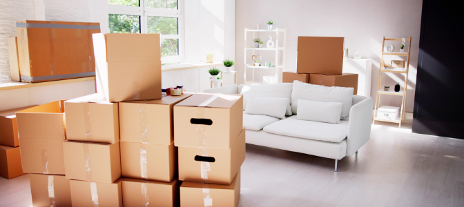 Sala iluminada com sofá branco e várias caixas de papelão organizadas, prontas para transporte durante uma mudança residencial
