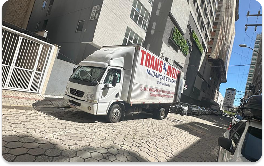 Caminhão de mudança residencial estacionado em frente a prédio urbano durante serviço de transporte de móveis.